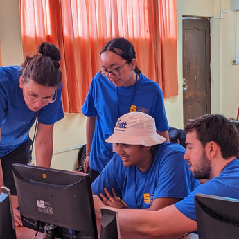 four students sitting in front of a computer monitor