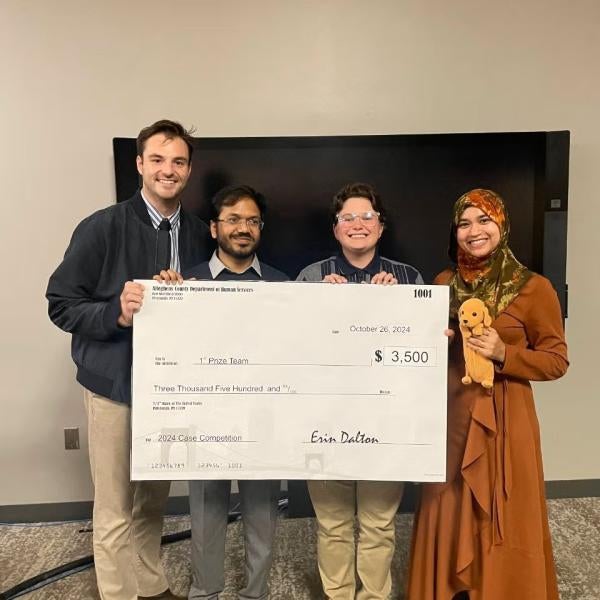 Photo of four people holding up a large check
