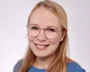 A blond woman wearing a blue sweater and glasses