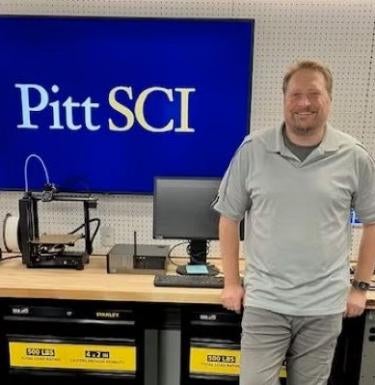 man wearing gray polo standing next to screen reading "Pitt SCI"
