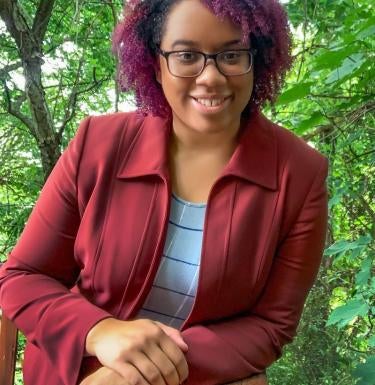 Photo of Dr. Angela Stewart Leaning on a Railing in Front of Trees
