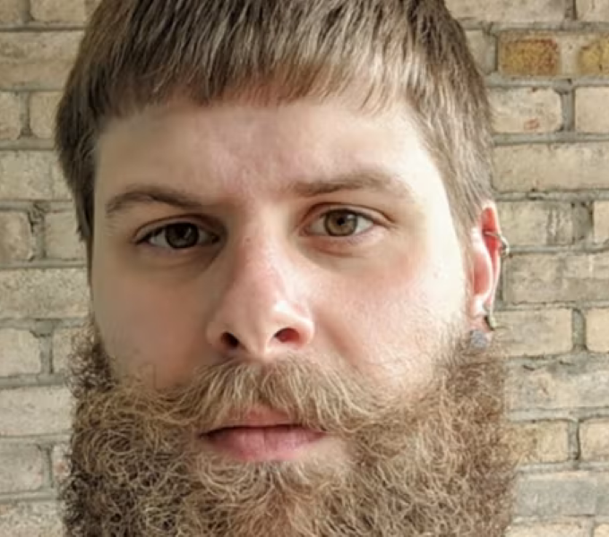 man with beard in front of beige brick wall